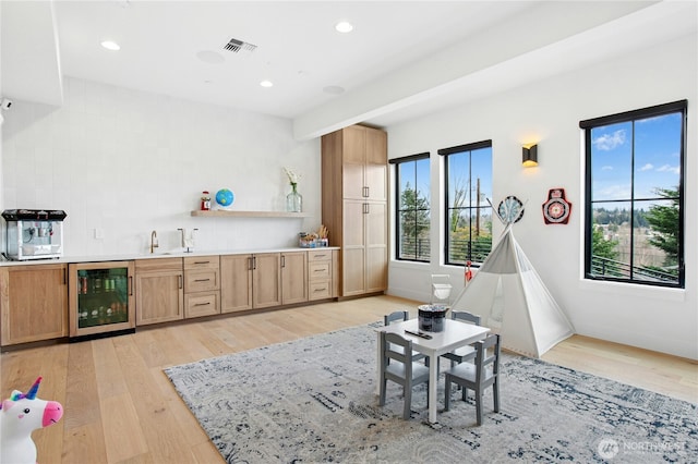 game room featuring beverage cooler, bar with sink, light wood-type flooring, and recessed lighting