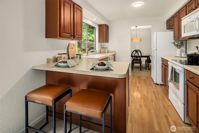 19924 31st Dr SE, Bothell, WA 98012 - kitchen featuring white appliances, a peninsula, light countertops, light wood-type flooring, and a kitchen breakfast bar