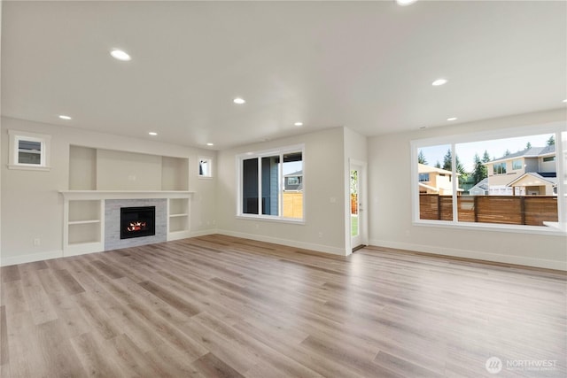 unfurnished living room featuring recessed lighting, light wood-style flooring, a warm lit fireplace, and baseboards