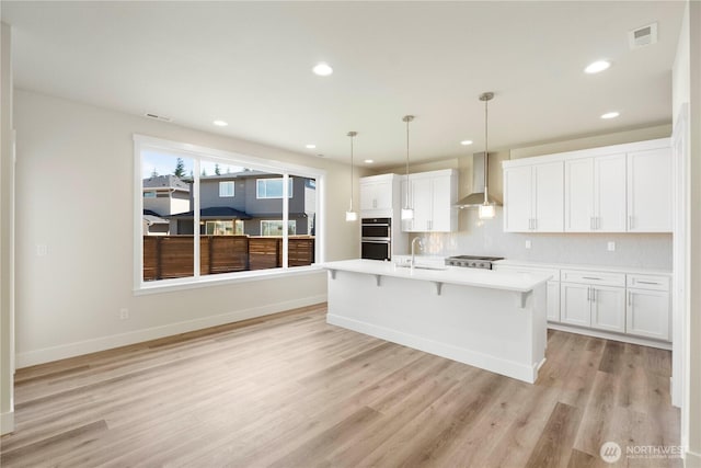 kitchen featuring wall chimney exhaust hood, a sink, light wood finished floors, light countertops, and white cabinets