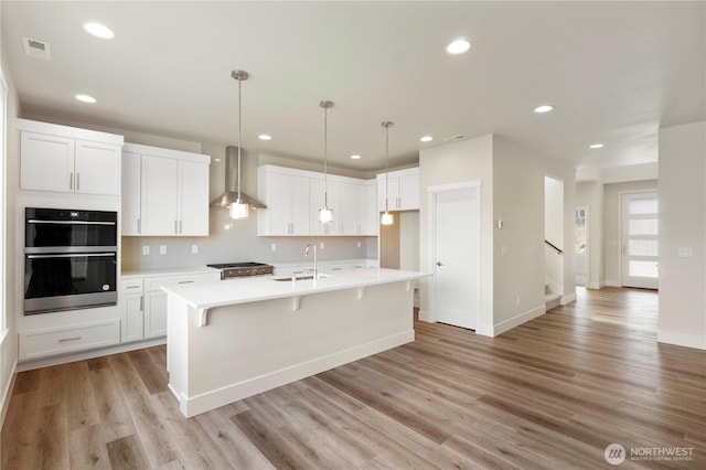 kitchen with wall chimney range hood, a sink, white cabinets, light countertops, and recessed lighting