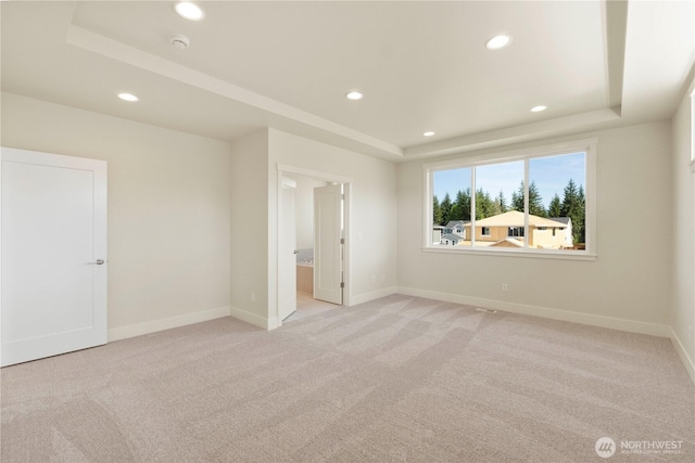 unfurnished bedroom featuring a raised ceiling, recessed lighting, light carpet, baseboards, and ensuite bathroom