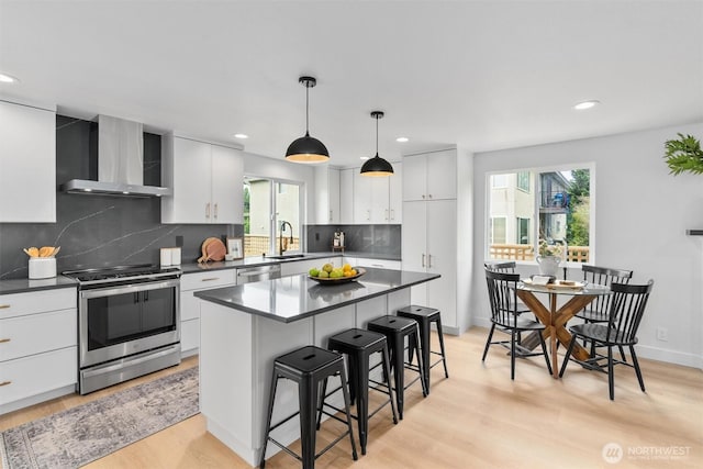 4257 33rd Ave W, Seattle, WA 98199 - kitchen with wall chimney exhaust hood, stainless steel appliances, a sink, dark countertops, and a breakfast bar