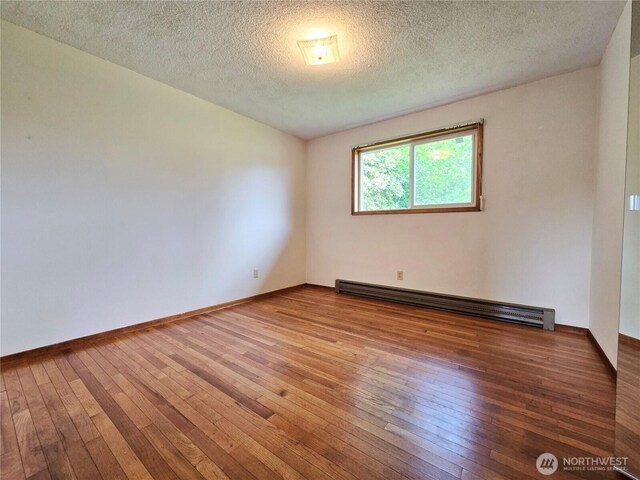 810 H St, Forks, WA 98331 - unfurnished room featuring a baseboard radiator, hardwood / wood-style flooring, a textured ceiling, and baseboards