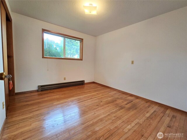 810 H St, Forks, WA 98331 - empty room featuring a baseboard radiator, light wood-style flooring, and baseboards