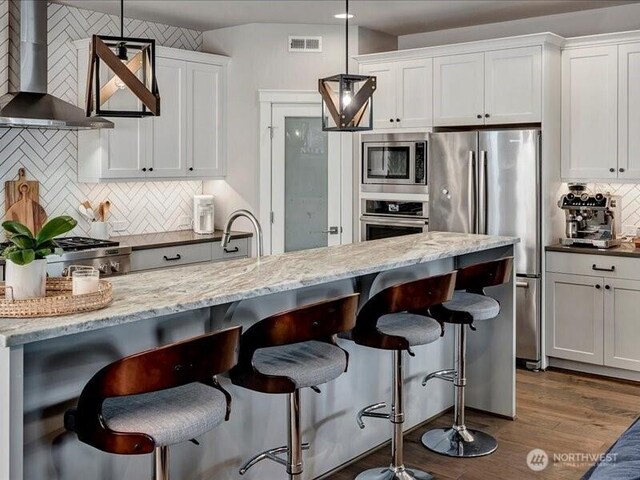 11550 174th Ave NE, Redmond, WA 98052 - kitchen featuring appliances with stainless steel finishes, wall chimney range hood, decorative backsplash, a kitchen bar, and white cabinetry
