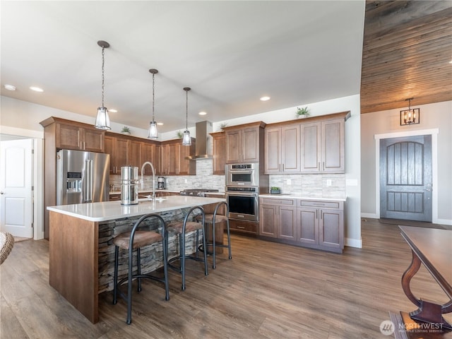 2611 Paisley St SE, East Wenatchee, WA 98802 - kitchen featuring appliances with stainless steel finishes, wall chimney range hood, light countertops, a center island with sink, and a breakfast bar area