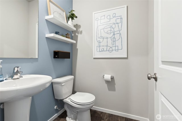 bathroom with baseboards, wood finished floors, toilet, and a sink