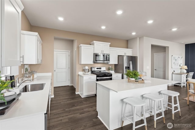 kitchen with stainless steel appliances, a sink, white cabinetry, dark wood-type flooring, and light countertops