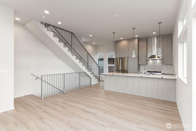 kitchen with freestanding refrigerator, wall chimney exhaust hood, light wood finished floors, decorative backsplash, and recessed lighting