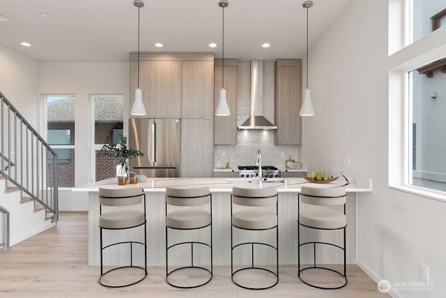 kitchen with freestanding refrigerator, modern cabinets, light countertops, wall chimney range hood, and tasteful backsplash