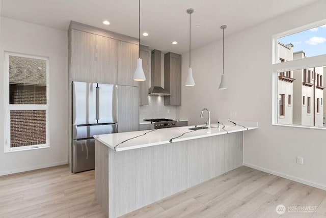 kitchen with wall chimney exhaust hood, freestanding refrigerator, a sink, light wood-style floors, and recessed lighting