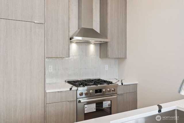 kitchen with stainless steel gas stove, wall chimney exhaust hood, modern cabinets, tasteful backsplash, and light countertops