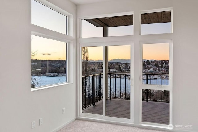 doorway with plenty of natural light, carpet flooring, a water view, and baseboards