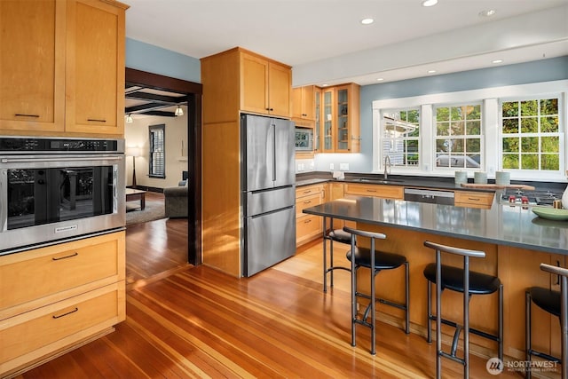 3227 37th Ave S, Seattle, WA 98144 - kitchen featuring appliances with stainless steel finishes, a sink, light wood-style flooring, glass insert cabinets, and a breakfast bar