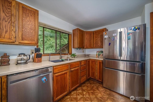 kitchen featuring stainless steel appliances, a sink, light countertops, and brown cabinets