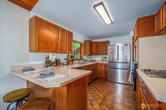 kitchen with appliances with stainless steel finishes, a peninsula, brown cabinetry, a sink, and light countertops
