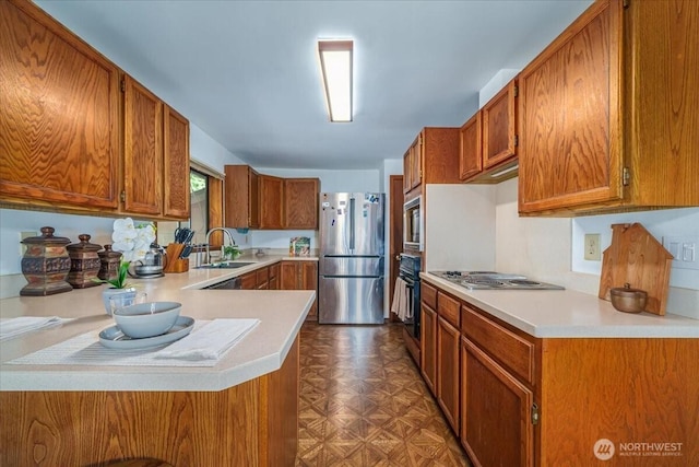 kitchen with appliances with stainless steel finishes, a sink, brown cabinetry, and light countertops