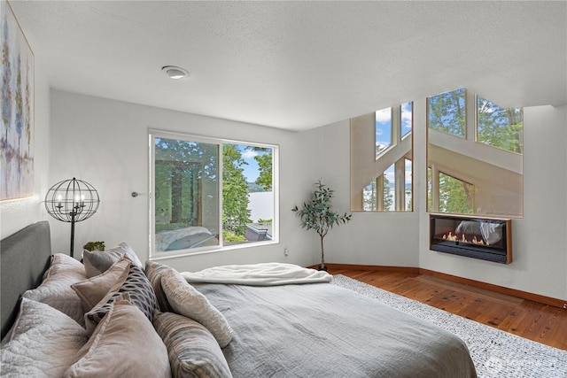 8526 E Mercer Way, Mercer Island, WA 98040 - bedroom featuring wood finished floors, a glass covered fireplace, a textured ceiling, and a chandelier