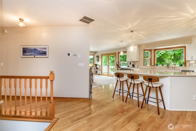 7509 145th St NW, Gig Harbor, WA 98329 - kitchen featuring white cabinets, light countertops, a kitchen breakfast bar, light wood finished floors, and hanging light fixtures