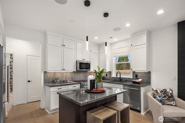 kitchen with appliances with stainless steel finishes, a sink, decorative backsplash, light wood finished floors, and white cabinetry