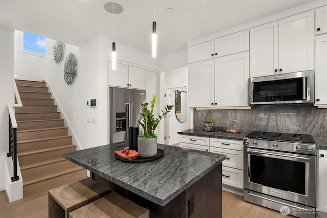 kitchen featuring appliances with stainless steel finishes, decorative backsplash, light wood-style floors, white cabinetry, and decorative light fixtures
