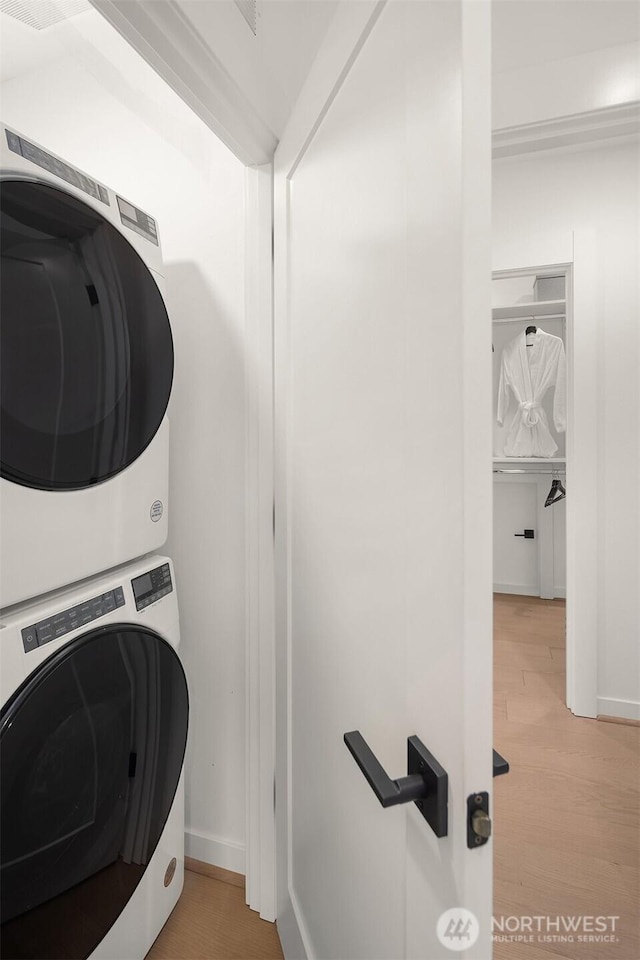 laundry room with stacked washer and clothes dryer, light wood-style flooring, and baseboards
