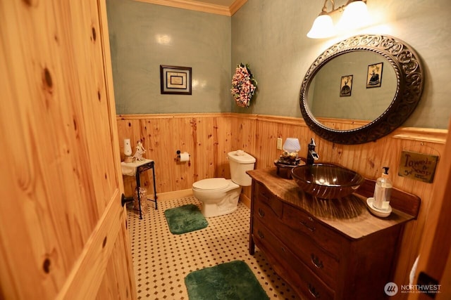bathroom with wainscoting, toilet, crown molding, vanity, and wooden walls
