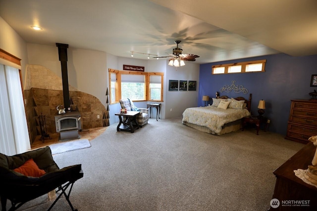 carpeted bedroom featuring a wood stove and ceiling fan
