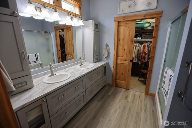 bathroom with a stall shower, wood finished floors, a spacious closet, and double vanity