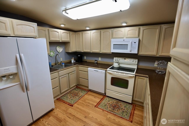 kitchen featuring white appliances, a sink, light wood-style floors, dark countertops, and lofted ceiling