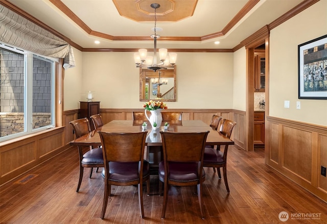 dining space with a tray ceiling, wainscoting, a chandelier, dark wood-style flooring, and ornamental molding