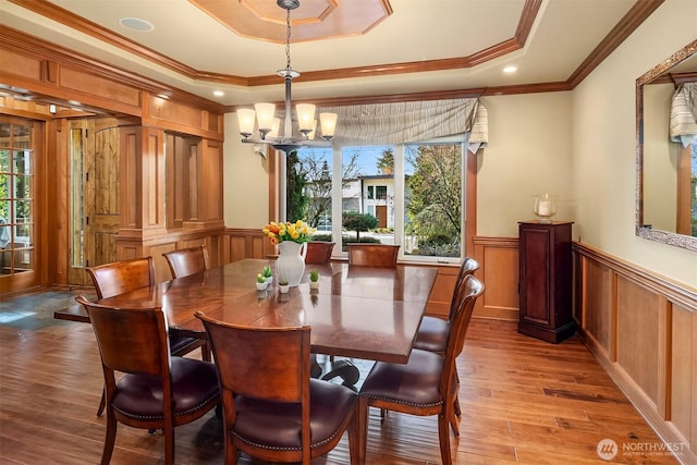 dining area with a raised ceiling, light wood-type flooring, a chandelier, crown molding, and a decorative wall