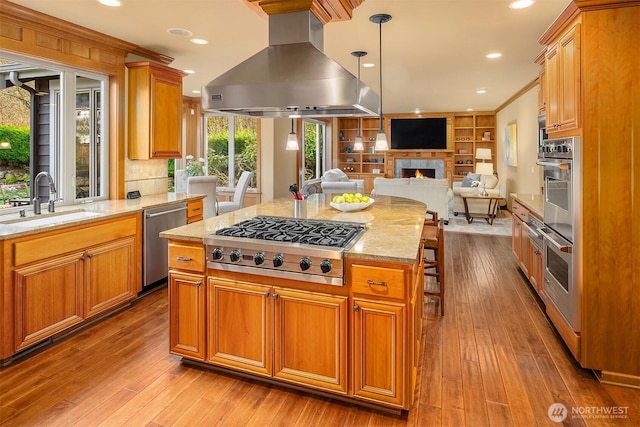 kitchen with island range hood, a sink, appliances with stainless steel finishes, open floor plan, and light stone countertops