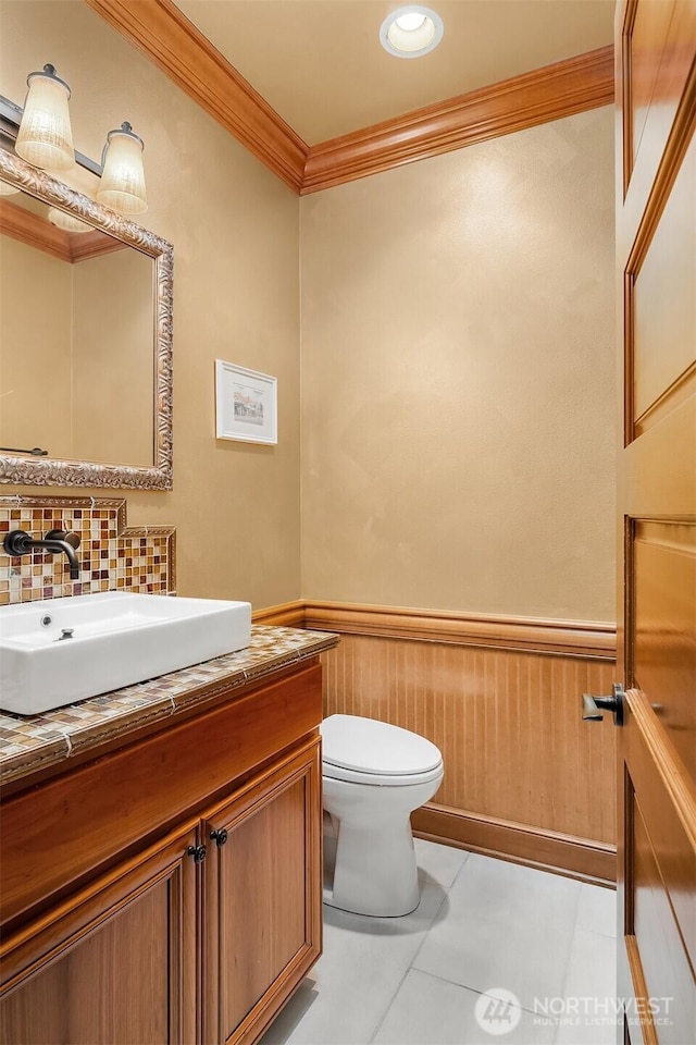 half bathroom with ornamental molding, wainscoting, vanity, decorative backsplash, and toilet