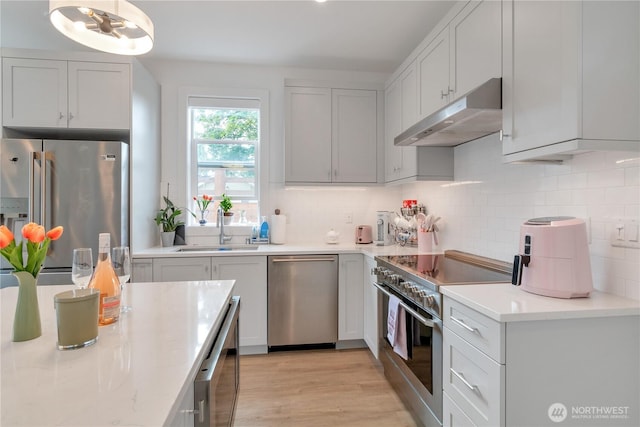 1415 29th Ave Unit C, Seattle, WA 98122 - kitchen with stainless steel appliances, under cabinet range hood, a sink, decorative backsplash, and light wood finished floors