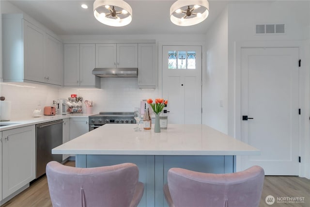 1415 29th Ave Unit C, Seattle, WA 98122 - kitchen with stainless steel appliances, under cabinet range hood, tasteful backsplash, a kitchen breakfast bar, and light wood-type flooring