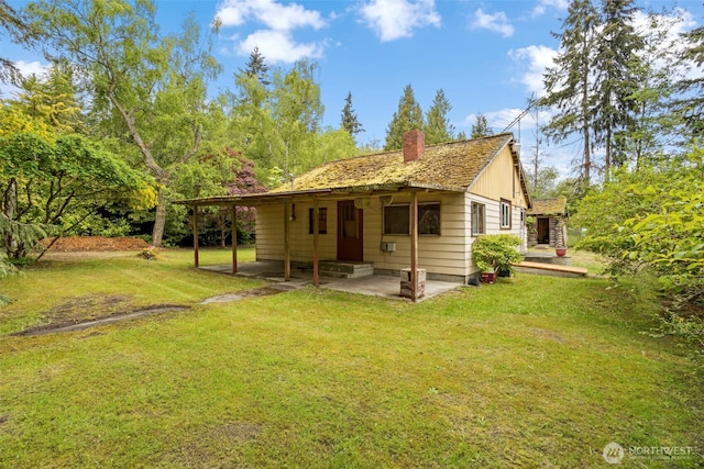 rear view of house featuring a patio, a chimney, and a lawn