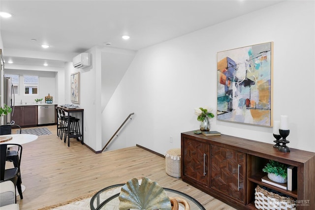 living area featuring a wall unit AC, light wood-style floors, recessed lighting, and baseboards