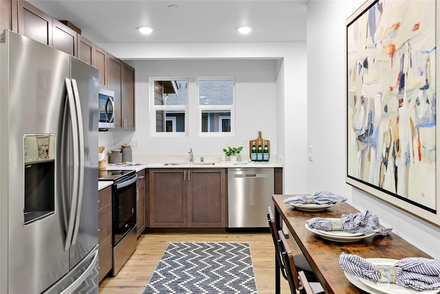 kitchen with appliances with stainless steel finishes, a sink, light countertops, light wood finished floors, and recessed lighting