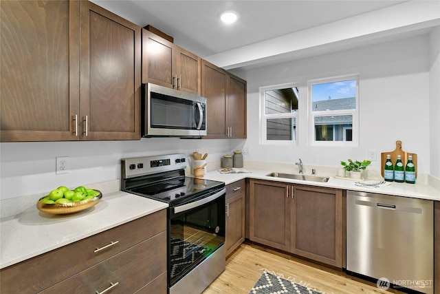 kitchen featuring appliances with stainless steel finishes, a sink, light wood-type flooring, dark brown cabinetry, and recessed lighting