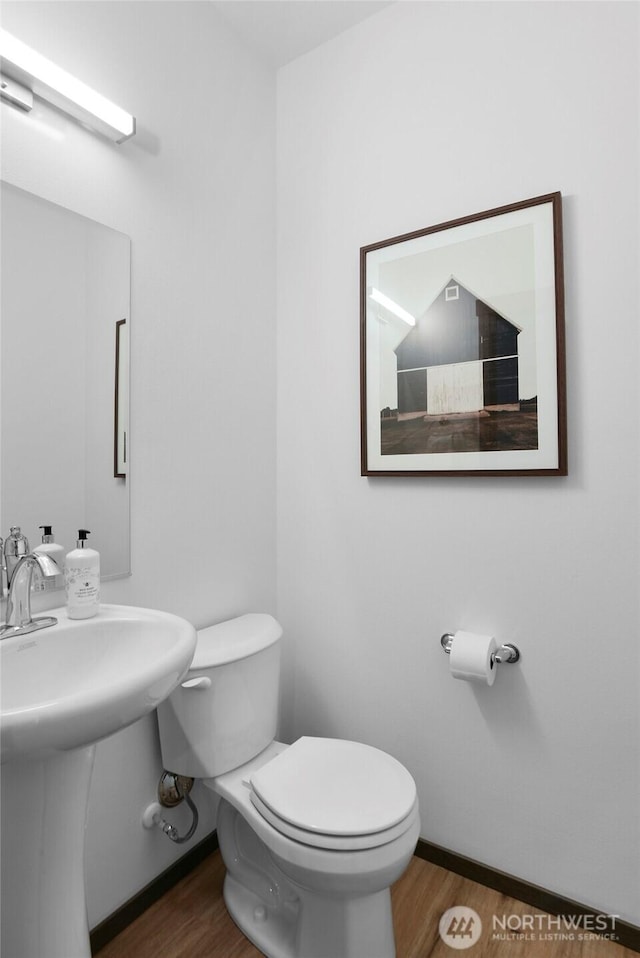 half bath with wood finished floors, toilet, baseboards, and a sink