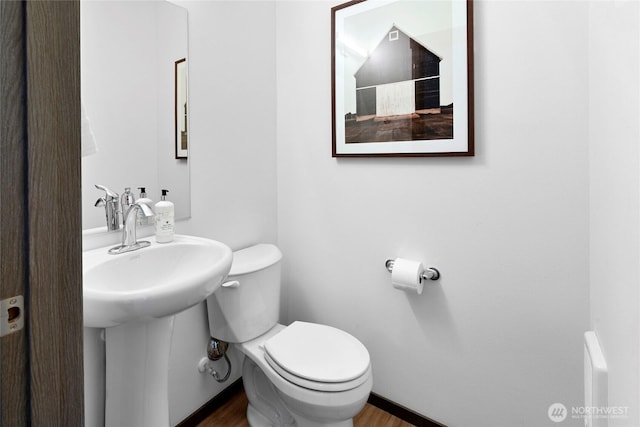 half bathroom with toilet, wood finished floors, and a sink