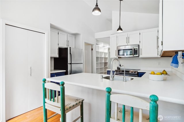 kitchen featuring stainless steel appliances, a peninsula, a sink, white cabinets, and lofted ceiling