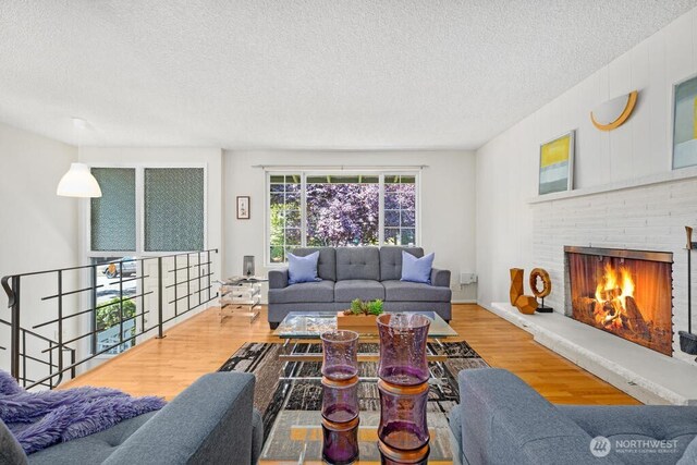 living area featuring a textured ceiling, wood finished floors, and a brick fireplace