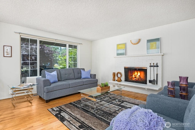 living room featuring a textured ceiling, wood finished floors, and a brick fireplace