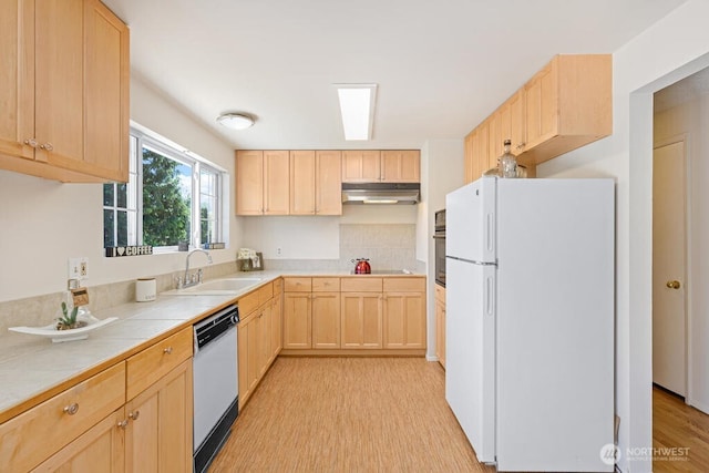 kitchen featuring white appliances, light brown cabinetry, a sink, under cabinet range hood, and light wood-style floors