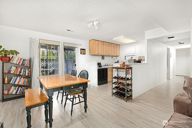 dining area with light wood-type flooring, a textured ceiling, and baseboards
