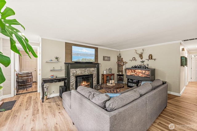 living area featuring a fireplace, light wood finished floors, baseboards, and ornamental molding