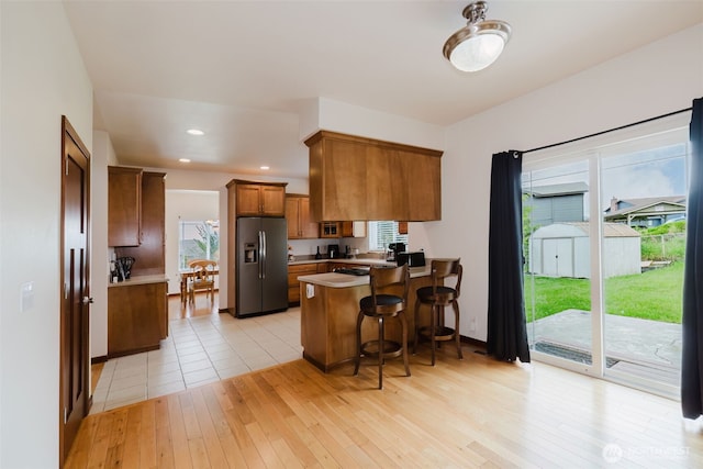 3323 Appaloosa Way, Bremerton, WA 98310 - kitchen with fridge with ice dispenser, brown cabinets, a peninsula, light wood finished floors, and a kitchen bar